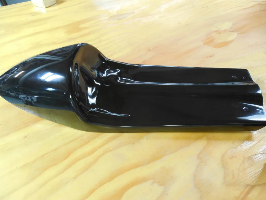 Black glossy car part with pointed nose cone on wooden surface