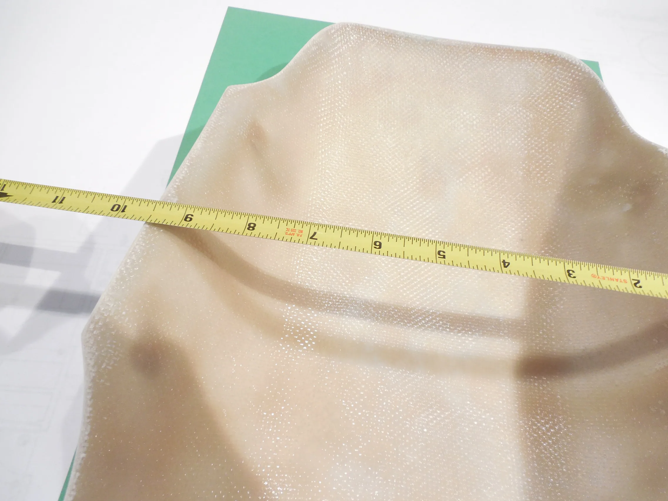 Cream-colored fabric measured with yellow tape measure on green and white surface