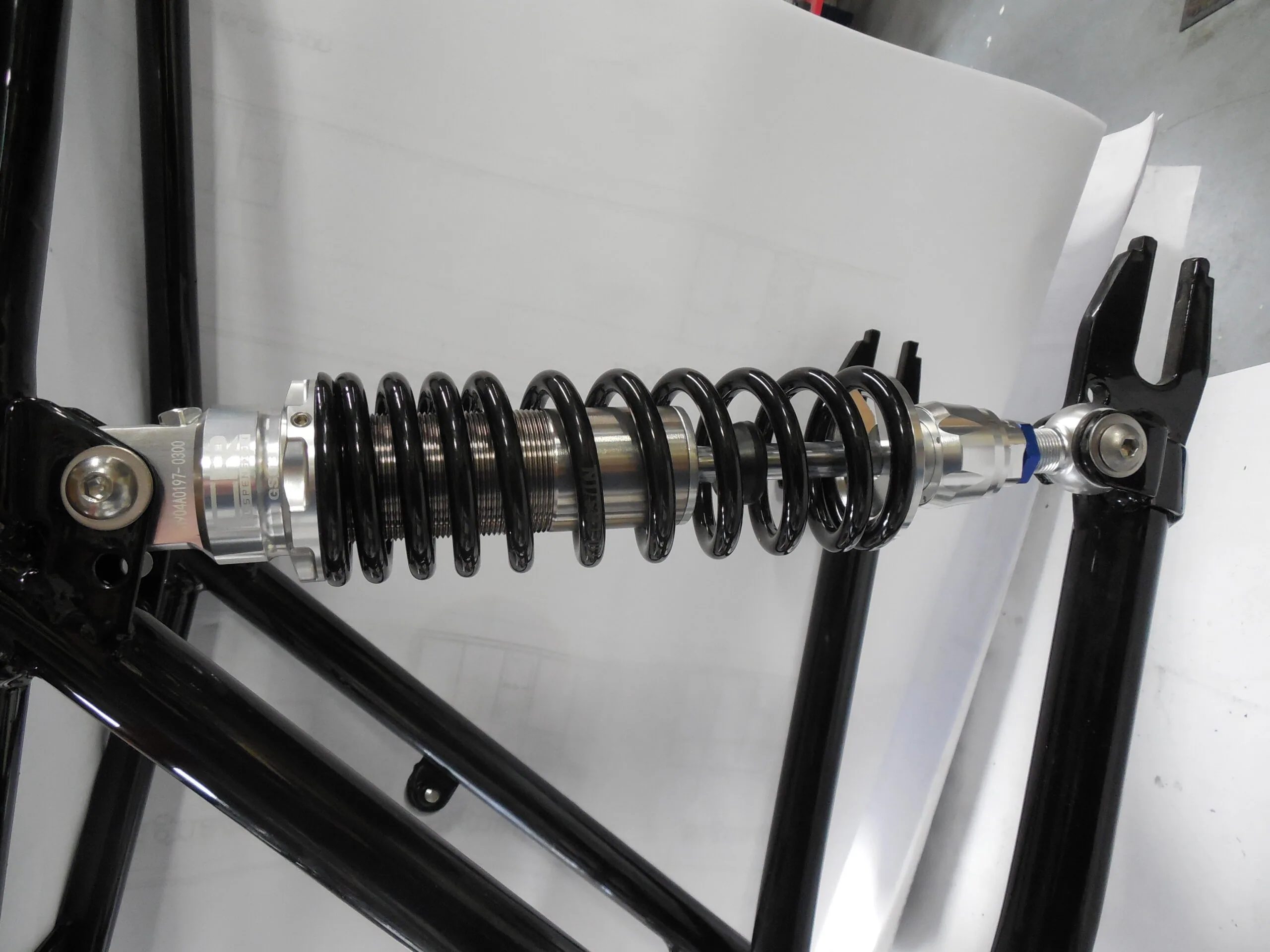 Motorcycle shock absorber assembly with black coil spring and metal mounting brackets on white background