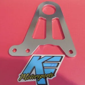 Gray metal bracket with circular opening and two rectangular slots mounted on pink surface with blue motorsports logo badge