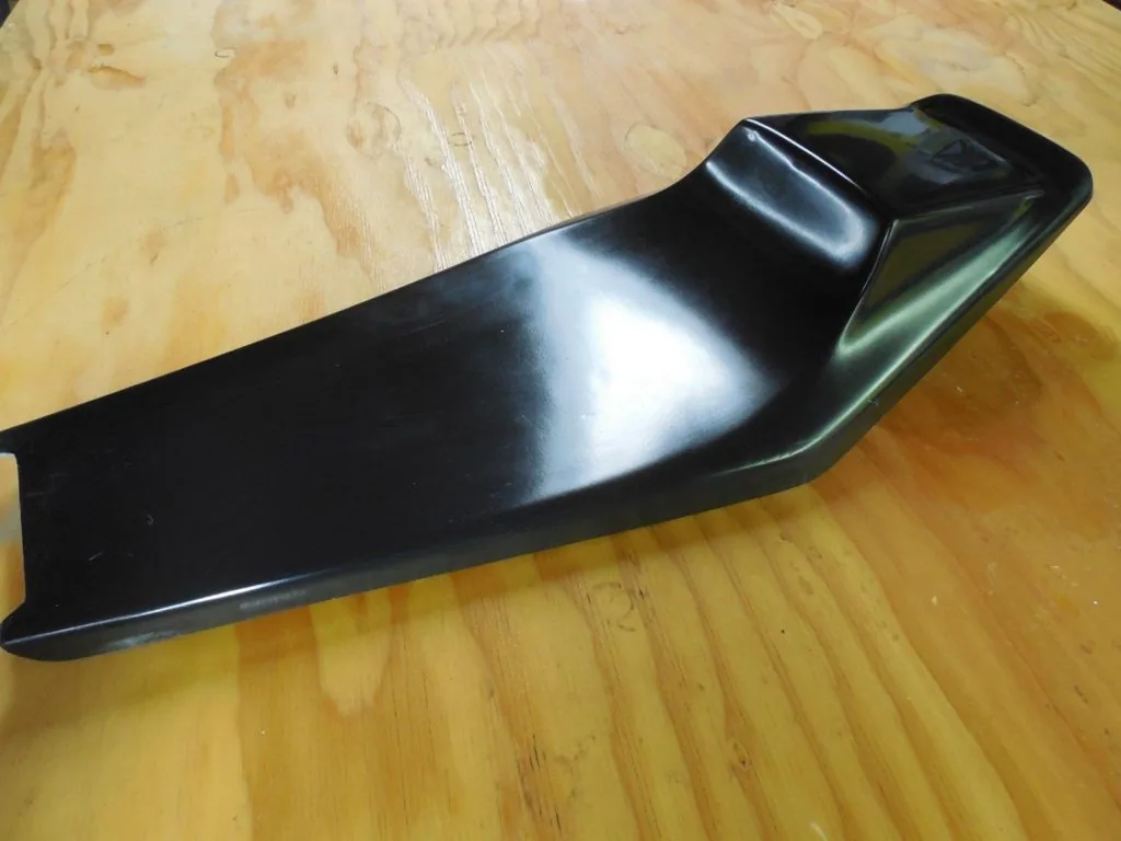 Black flat-track style motorcycle seat with curved design on wooden floor