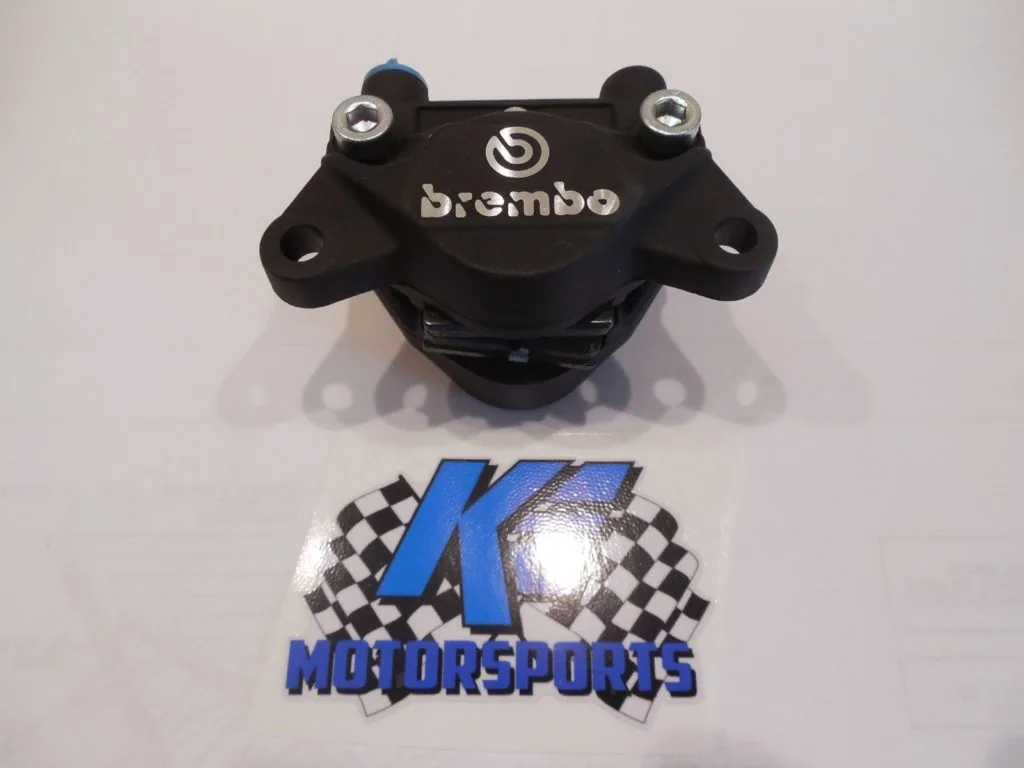 Black Brembo brake caliper with mounting bolts displayed above motorsports logo