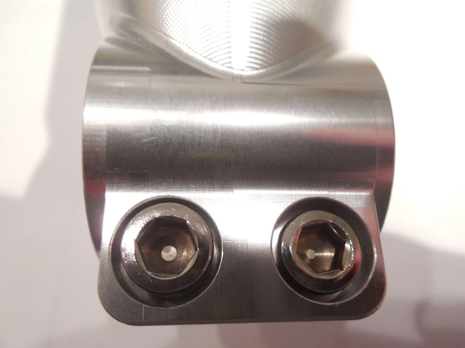 Polished metal bicycle stem with two socket head cap screws viewed from below against white background.