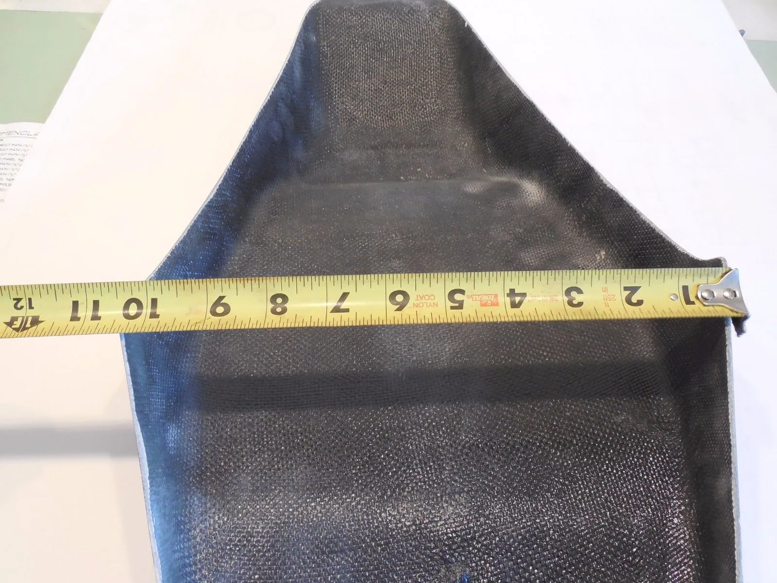 Black fabric storage container measured with yellow tape ruler on white surface