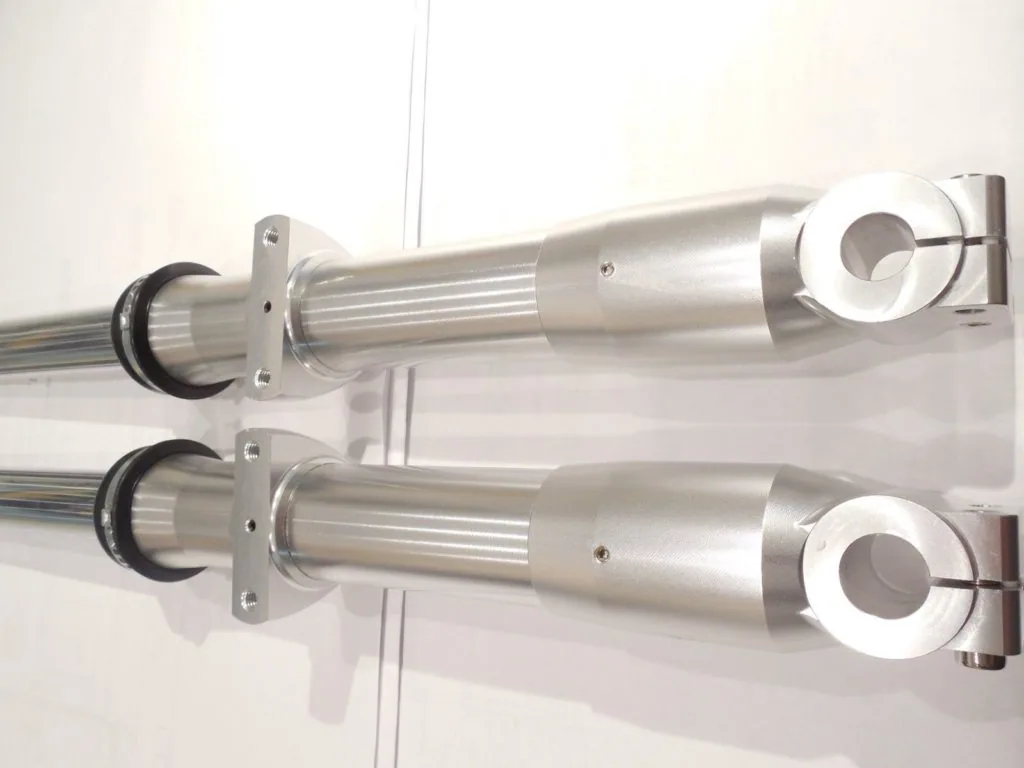 Two stainless steel cylindrical hydraulic dampers mounted vertically with black seals and mounting brackets