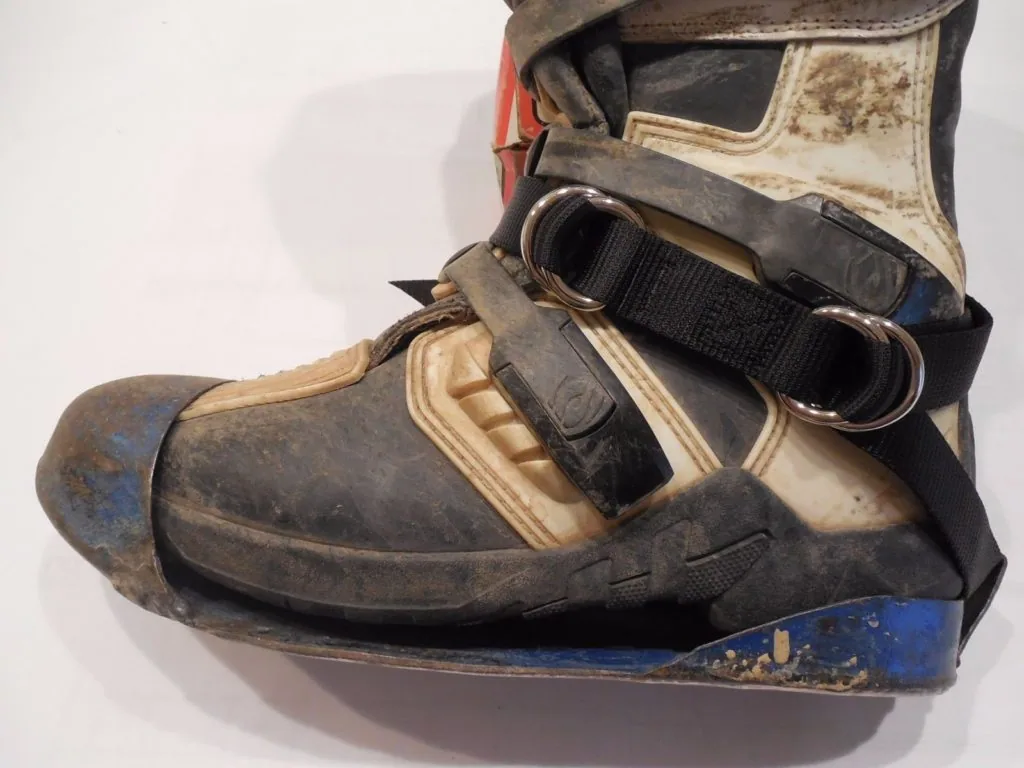 Worn brown and cream water sports boot with black ankle strap and metal D-ring, showing scuff marks and weathering on sole and upper