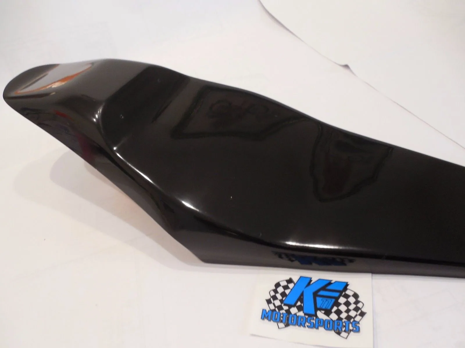 Black motorcycle seat with contoured design and grip panels on white surface