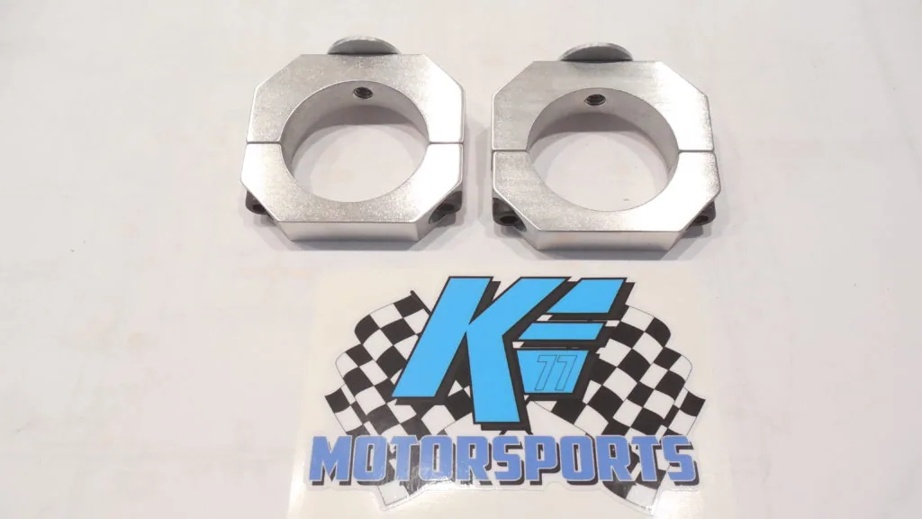 Two silver hexagonal metal clamps with circular openings and black screws, displayed above a K.E. Motorsports logo with checkered flag design