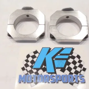 Two silver hexagonal metal clamps with circular openings and black screws, displayed above a K.E. Motorsports logo with checkered flag design