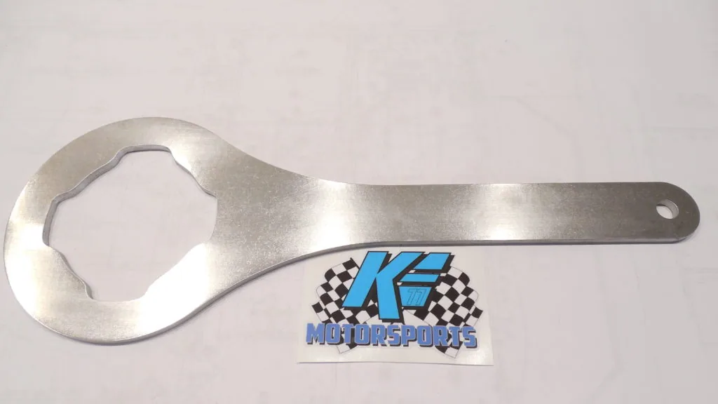 Metal wrench tool with octagonal socket head next to motorsports logo sticker on white background