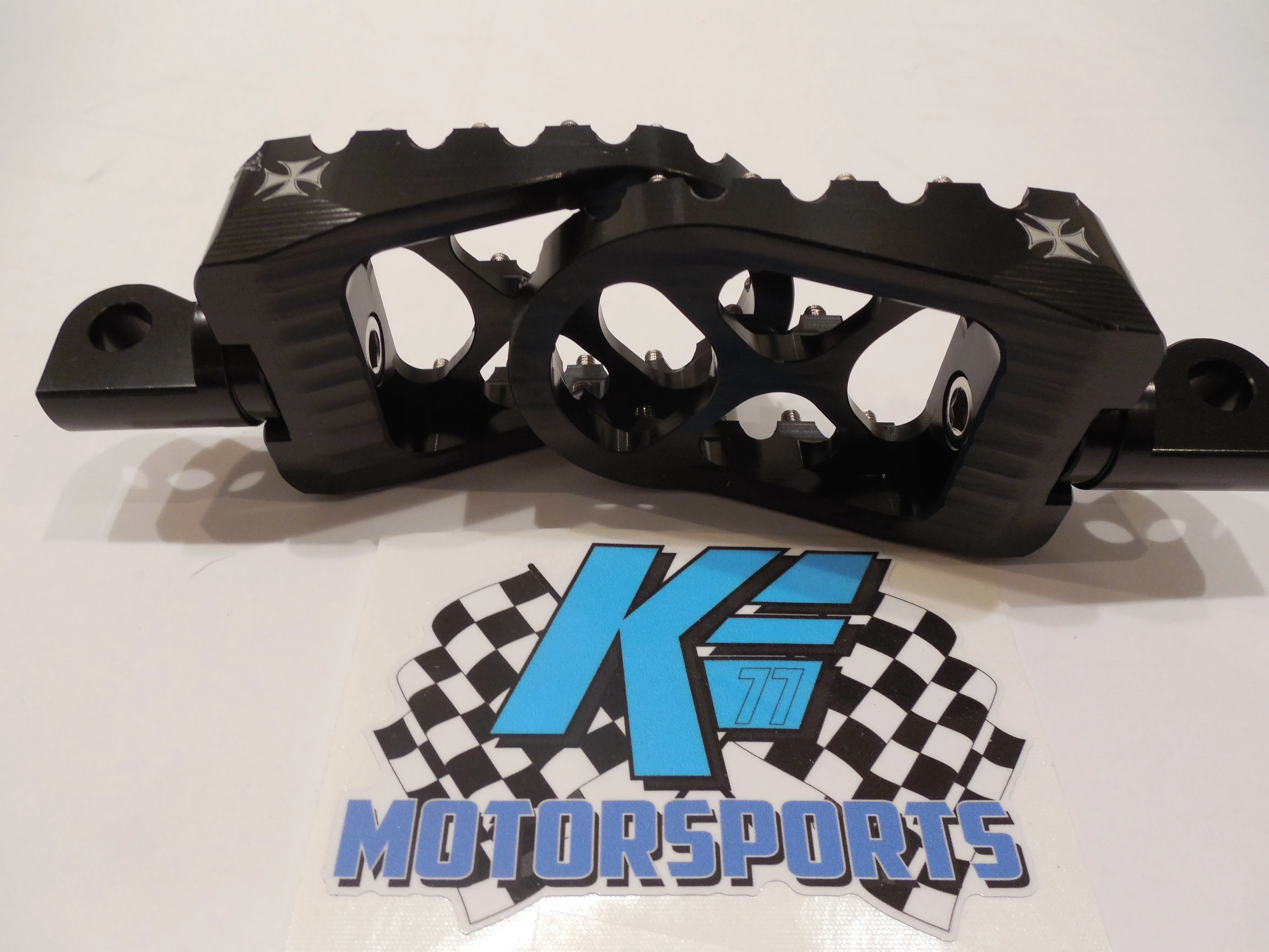 Black motorcycle brake caliper with cross design and checkered flag motorsports logo on white background