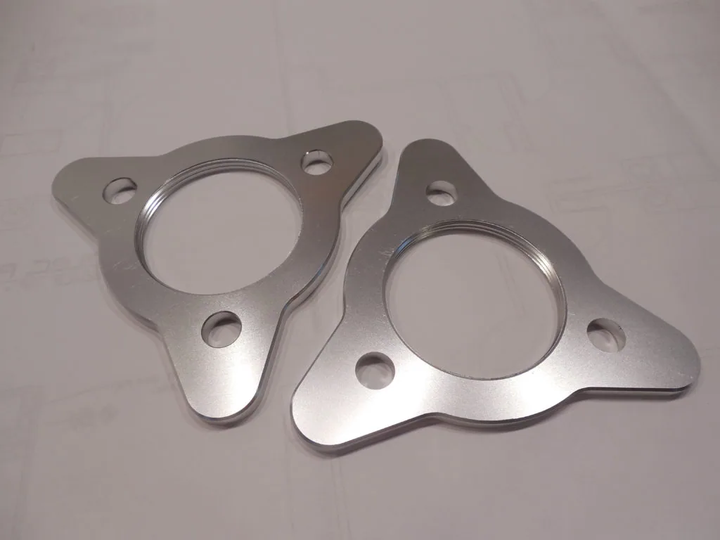 Two metallic flanges with circular center openings and mounting holes on a light background