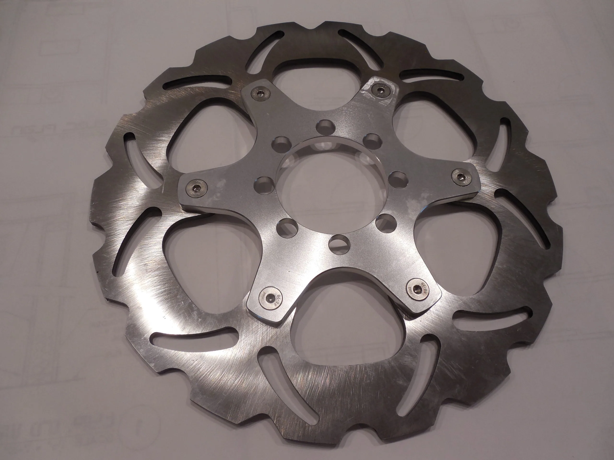 Polished metal brake rotor with scalloped edges and bolt holes on neutral background