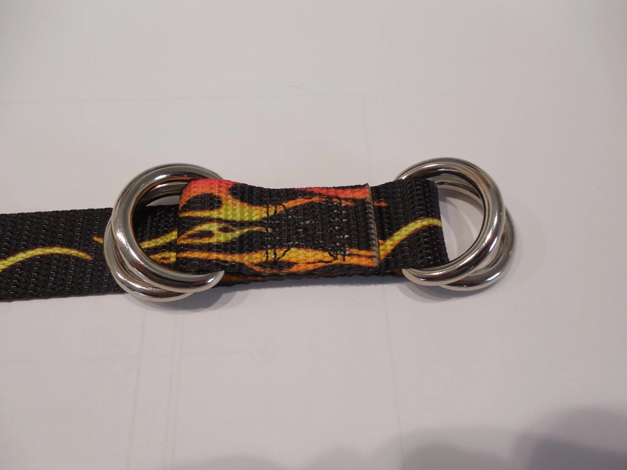 Black nylon belt with red and yellow flame pattern and dual metal D-rings on neutral background