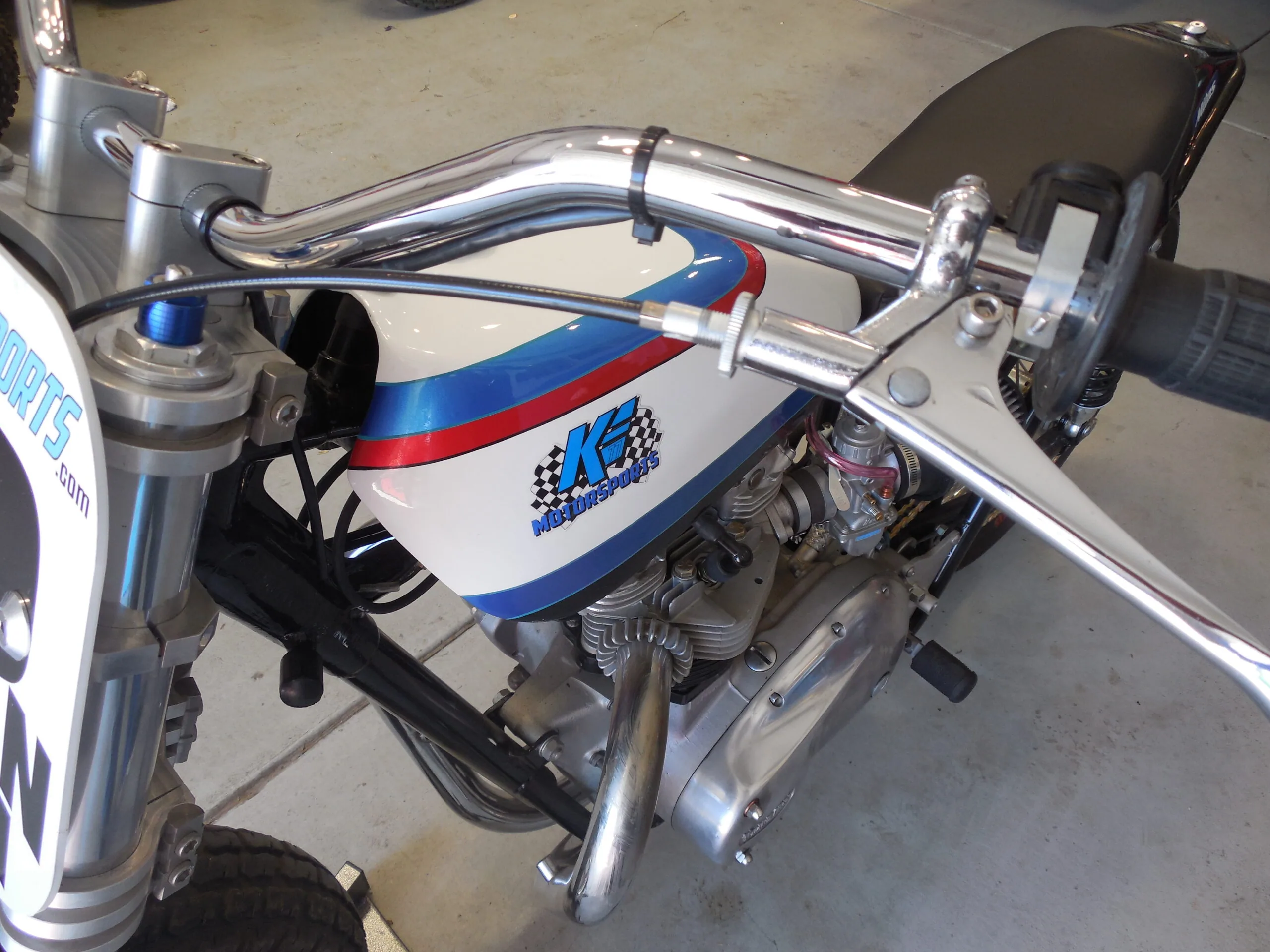Custom motorcycle with chrome handlebars, white blue and red tank, and exposed engine on concrete floor