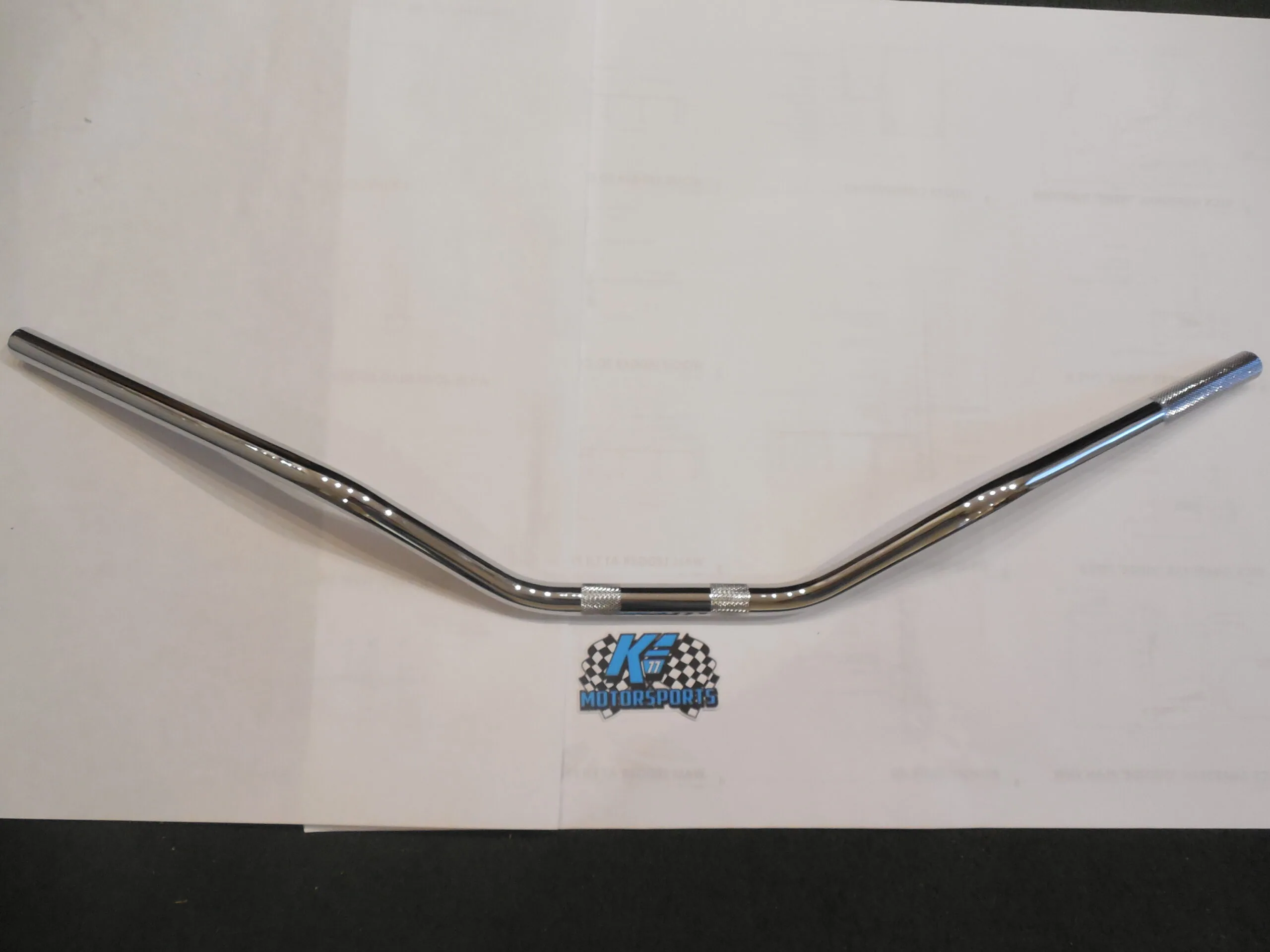 Chrome motorcycle handlebar with rise, center knurled grips, flat white background