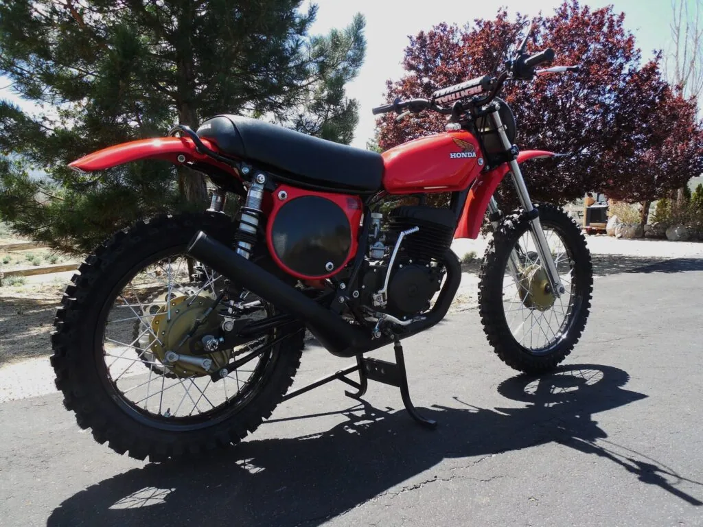 Red vintage dirt bike with red side panels and a black seat on a stand